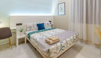 A neatly arranged bedroom with a bed, a bedside table, a chair, and a wall-mounted artwork.