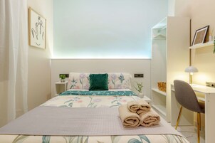 Um quarto arrumado com cama, mesas de cabeceira, escrivaninha e cadeira.