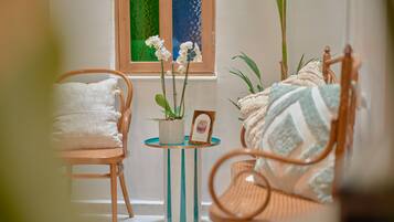 Um quarto aconchegante com uma cadeira de madeira, uma mesa de cabeceira listrada e uma janela com cortinas estampadas em verde e azul.