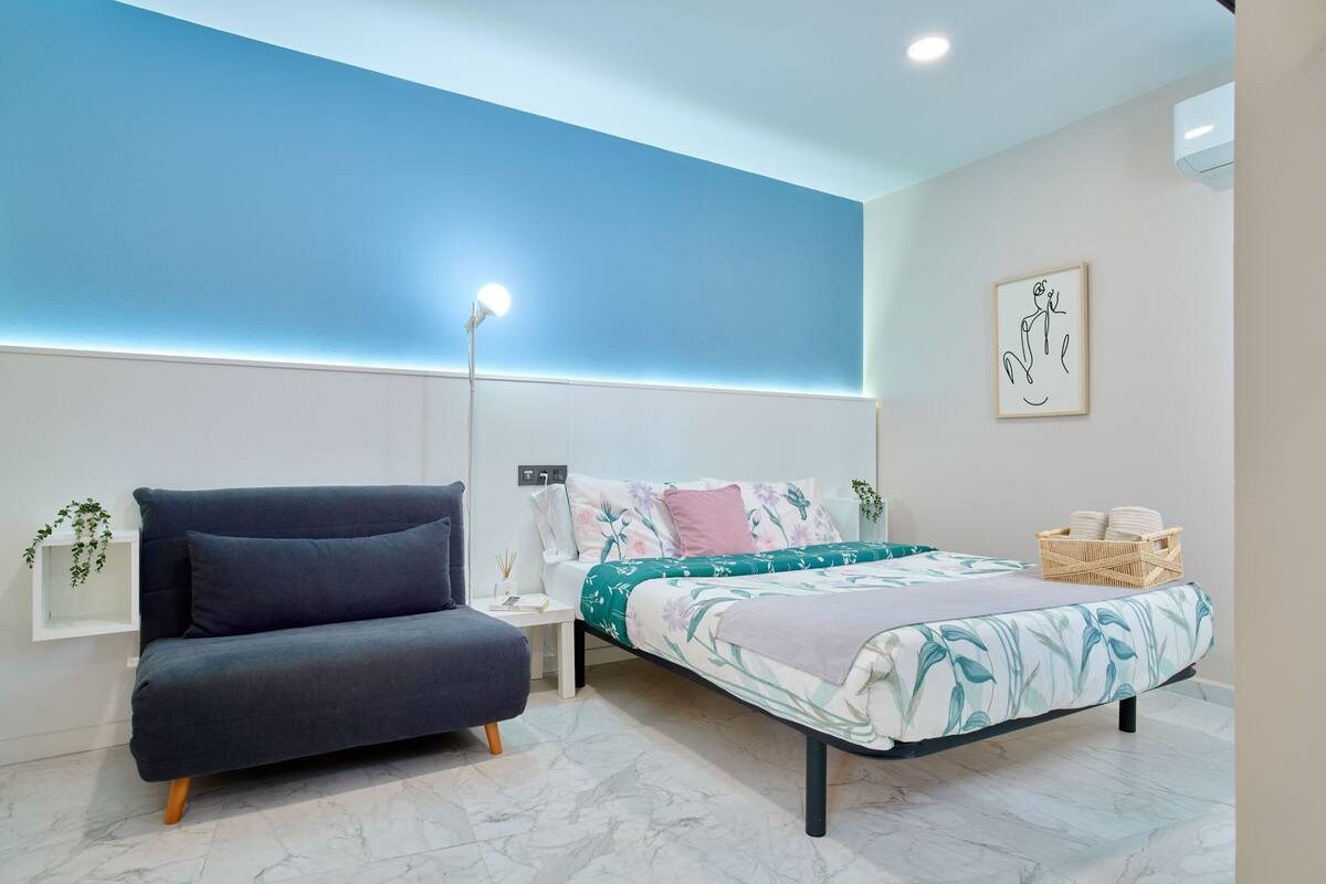 Une chambre à coucher moderne comprenant un lit, un canapé, une table de chevet et une étagère fixée au mur.