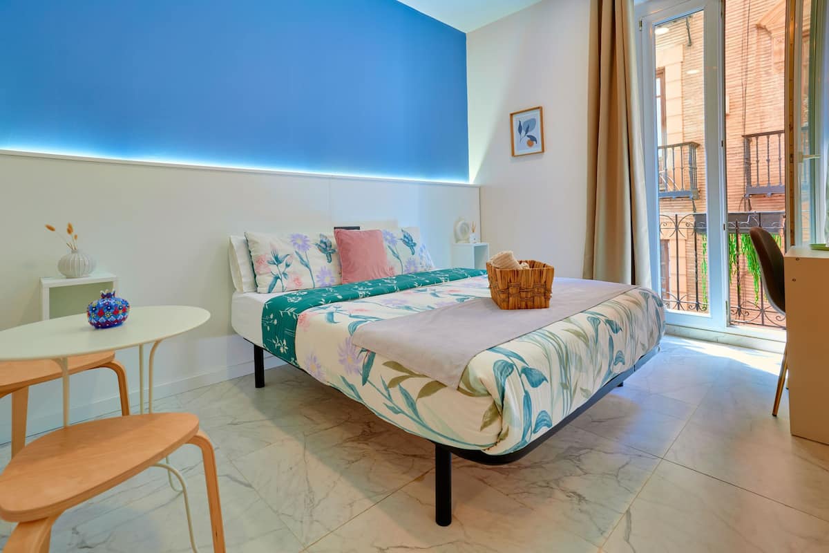 Une chambre à coucher avec un lit, une petite table et une chaise. Il y a une fenêtre donnant sur l’extérieur.