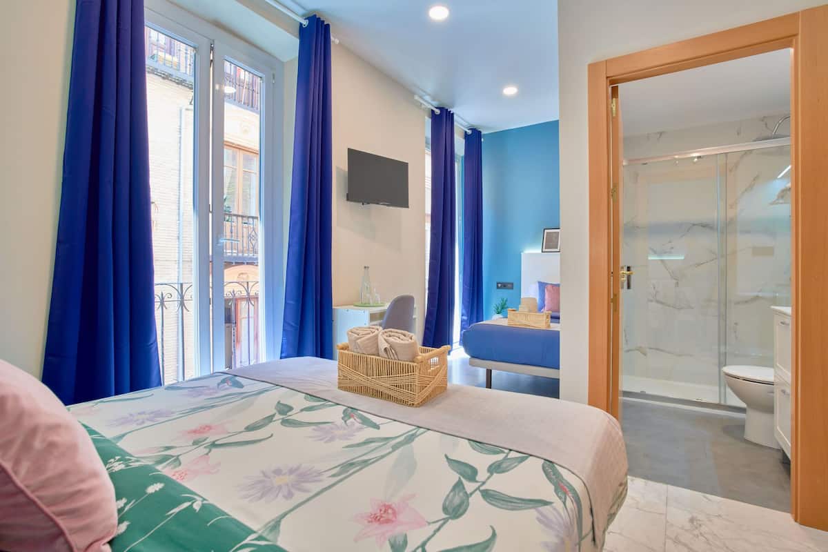 Une chambre d’hôtel avec un lit, une petite table avec un panier, une télévision et un espace douche.