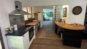 Cocina compacta con estufa, horno y un refrigerador pequeño. Cuenta con una encimera de madera y una escalera apoyada en la pared.