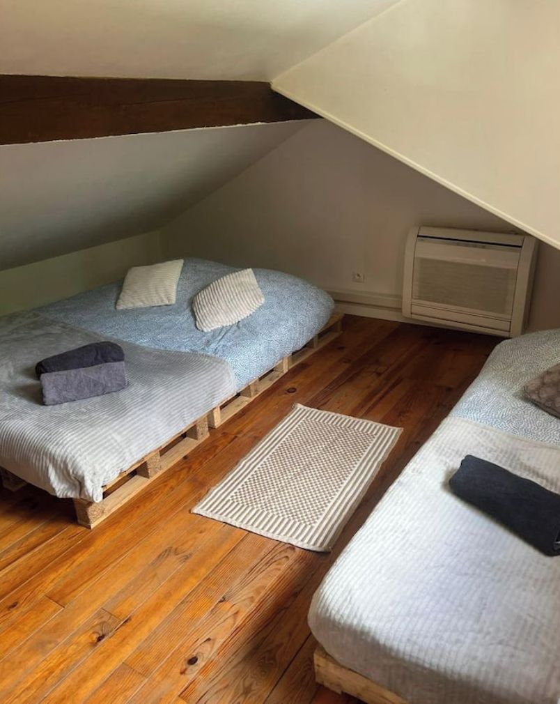 A small, cozy room with two beds, a wooden floor, and a slanted ceiling.