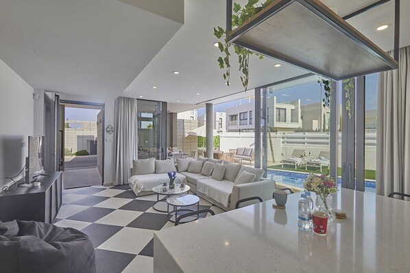 Relax in a spacious room with a large seating area, dining table, and bar, offering a view of the outdoor pool and surrounding buildings.