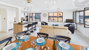 Een moderne keuken met een centraal eiland, een eethoek met een houten tafel voor vier personen, en een zithoek met een bank en stoelen.