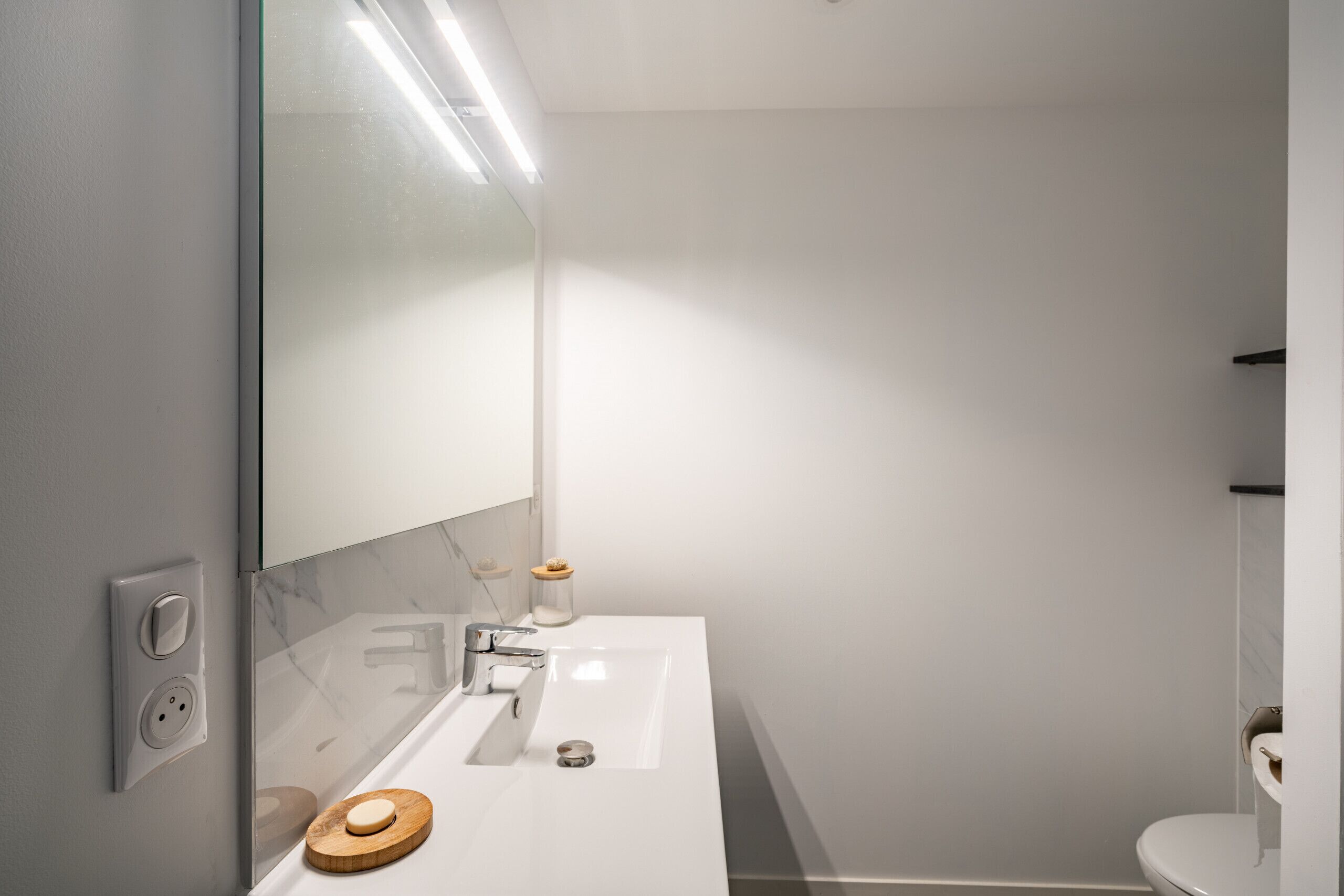 A modern bathroom with a white sink, mirror, and toilet.