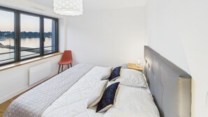 Een moderne slaapkamer met een groot raam, een rode stoel, een bed met wit beddengoed en een bijzondere hanglamp.