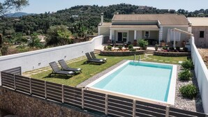 Ein Pool mit Liegestühlen, eine Terrasse mit Gartenmöbeln und Blick auf eine Hügelkette mit Gebäuden.