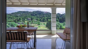 Ein Balkon mit Esstisch, Stuhl und Blick auf eine üppige grüne Landschaft mit Hügeln und Gebäuden in der Ferne.