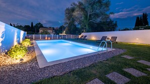 Ein rechteckiger Pool mit integrierter Leiter, umgeben von einem Kiesstreifen und einer Rasenfläche mit einigen Pflanzen.