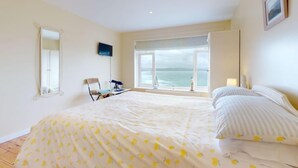 Une chambre avec un grand lit, une chaise, un téléviseur et une fenêtre donnant sur la mer.