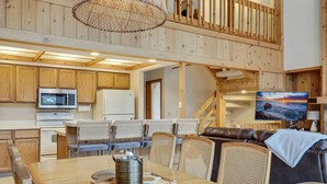 A spacious kitchen with wooden cabinets, a dining area with a table and chairs, and a cozy seating area with a sofa and a painting of a sunset. - Hamlet Village Chalet at Nubs Nob/ 4 bedrooms sleeps 12 (Harbor Springs)
