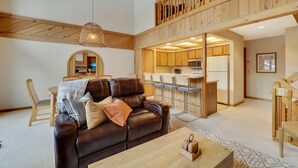 A spacious living area with a leather sofa, wooden dining table, and a kitchen in the background. - Hamlet Village Chalet at Nubs Nob/ 4 bedrooms sleeps 12 (Harbor Springs)