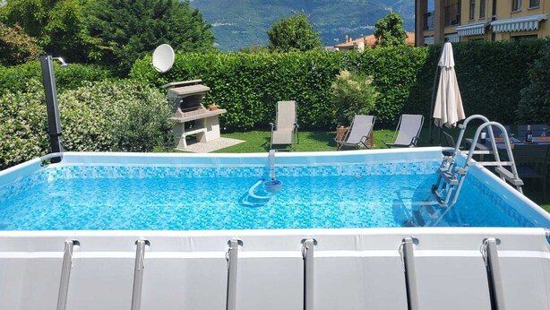 A swimming pool with lounge chairs and a barbecue area, surrounded by greenery and mountains in the background. - Two Steps from the Lake (Colico)