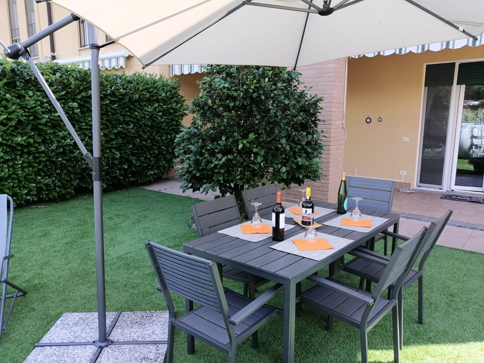 Un patio al aire libre con una mesa preparada para dos personas, rodeado de sillas y cubierto por un gran paraguas.