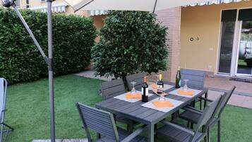 Un patio al aire libre con una mesa preparada para dos personas, rodeado de sillas y cubierto por un gran paraguas.