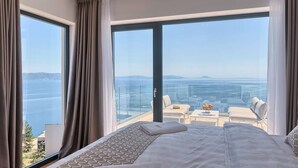 A hotel room with a large bed, a balcony with a view of the sea, and a small seating area with a table and chairs. - Villa Ateneum with sea view, jacuzzi&infinity pool (Ripenda Kosi)