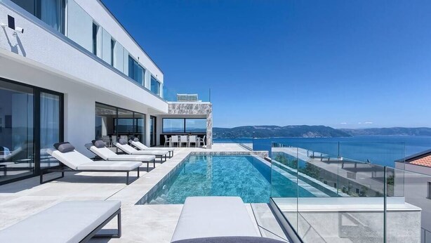 A modern infinity pool with clear blue water, surrounded by white lounge chairs and a glass balustrade. - Villa Ateneum with sea view, jacuzzi&infinity pool (Ripenda Kosi)