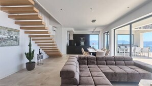 A modern living space with a staircase, a sectional sofa, and a dining area with a view. - Villa Ateneum with sea view, jacuzzi&infinity pool (Ripenda Kosi)