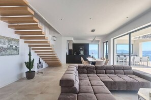 A modern living space with a staircase, a sectional sofa, and a dining area with a view.