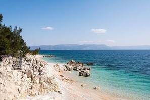 A rocky beach with clear water, steps leading down to the shore, and distant mountains.