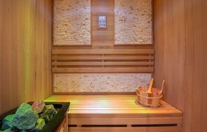 A sauna with wooden benches, a control panel, and a wooden bucket with a brush.