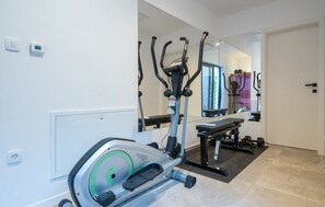 Une salle de sport à domicile équipée d’un appareil elliptique, d’un banc et d’un miroir qui reflète la pièce.