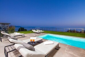 Un espace aménagé au bord de la piscine, avec des chaises longues et une piscine, donnant sur une étendue d’eau.