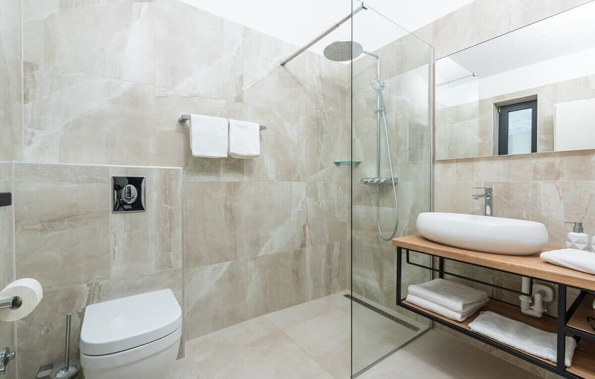 Une salle de bain moderne avec une douche à parois de verre, des toilettes blanches, un grand lavabo et un miroir au-dessus du lavabo.