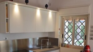 A modern kitchen with white cabinetry, a stainless steel sink, and a built-in oven. - Villa Paola - Fontane Bianche (Fontane Bianche)