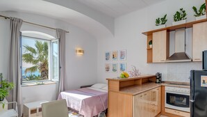 Habitación de hotel compacta con kitchenette, zona de comedor y cama con vista a palmeras.