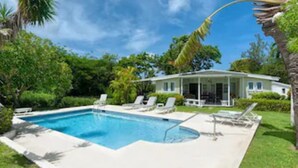 A swimming pool with lounge chairs, a house with a covered patio, and lush greenery.