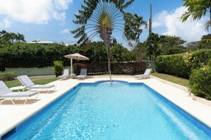 Une piscine rectangulaire à l’eau d’un bleu cristallin, entourée de chaises longues blanches et agrémentée d’un seul parasol.