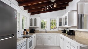A modern kitchen with white cabinetry, a stainless steel refrigerator, a built-in oven, and a large island with a sink.