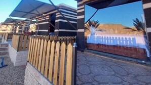 Área externa coberta com cerca de madeira, piso estampado e vista para uma colina.