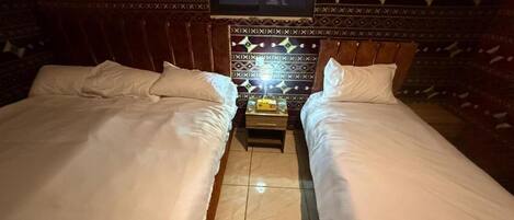 A room with two beds, a small table with a lamp, and patterned walls.