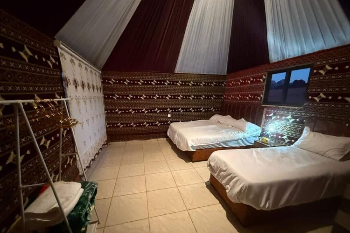 Una habitació amb dos llits, una petita televisió i parets amb un disseny decoratiu.