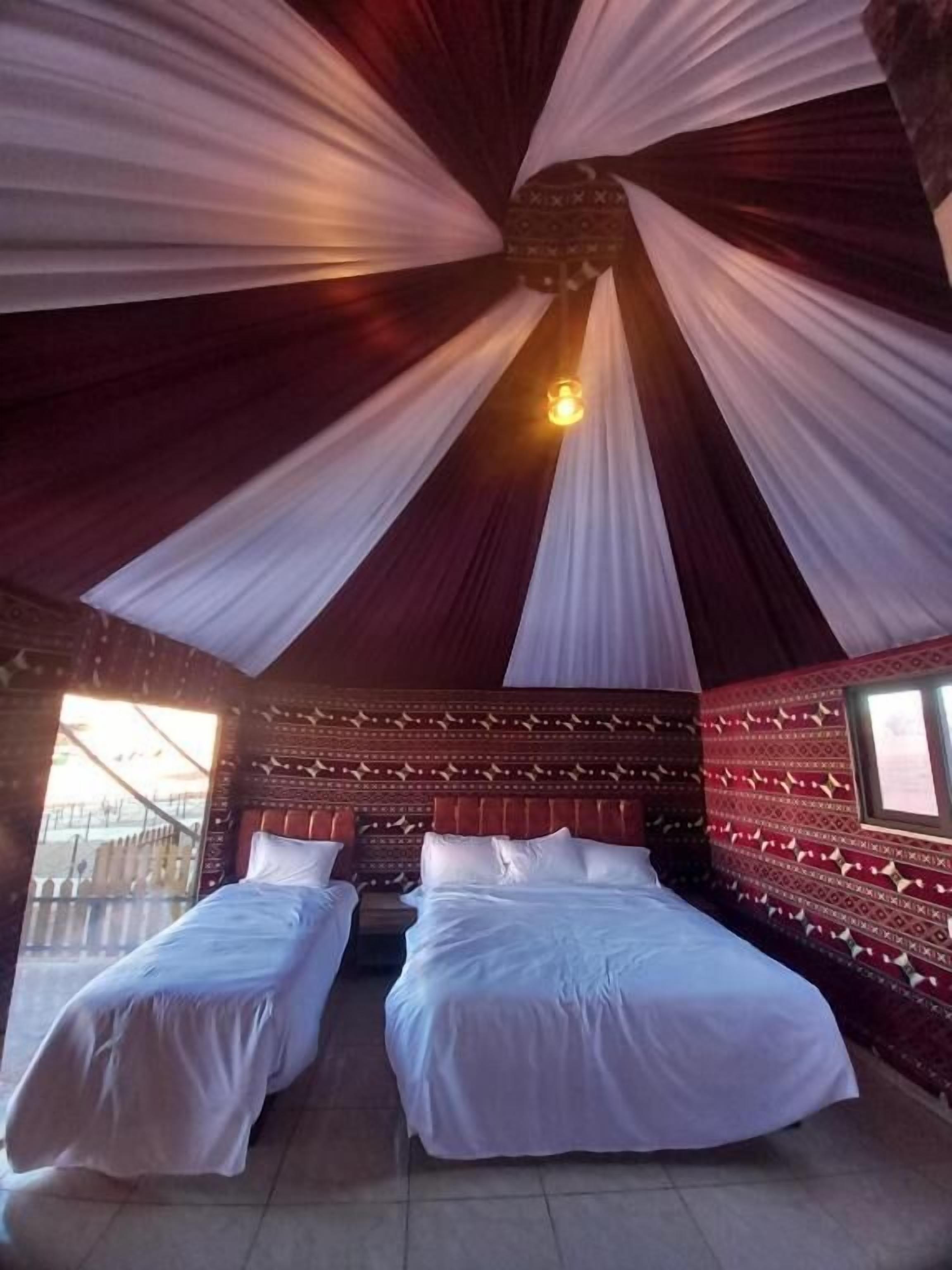 A room with two beds, a patterned wall, and a ceiling with draped fabric.