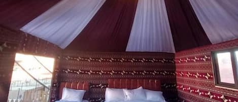A room with two beds, a patterned wall, and a ceiling with draped fabric.