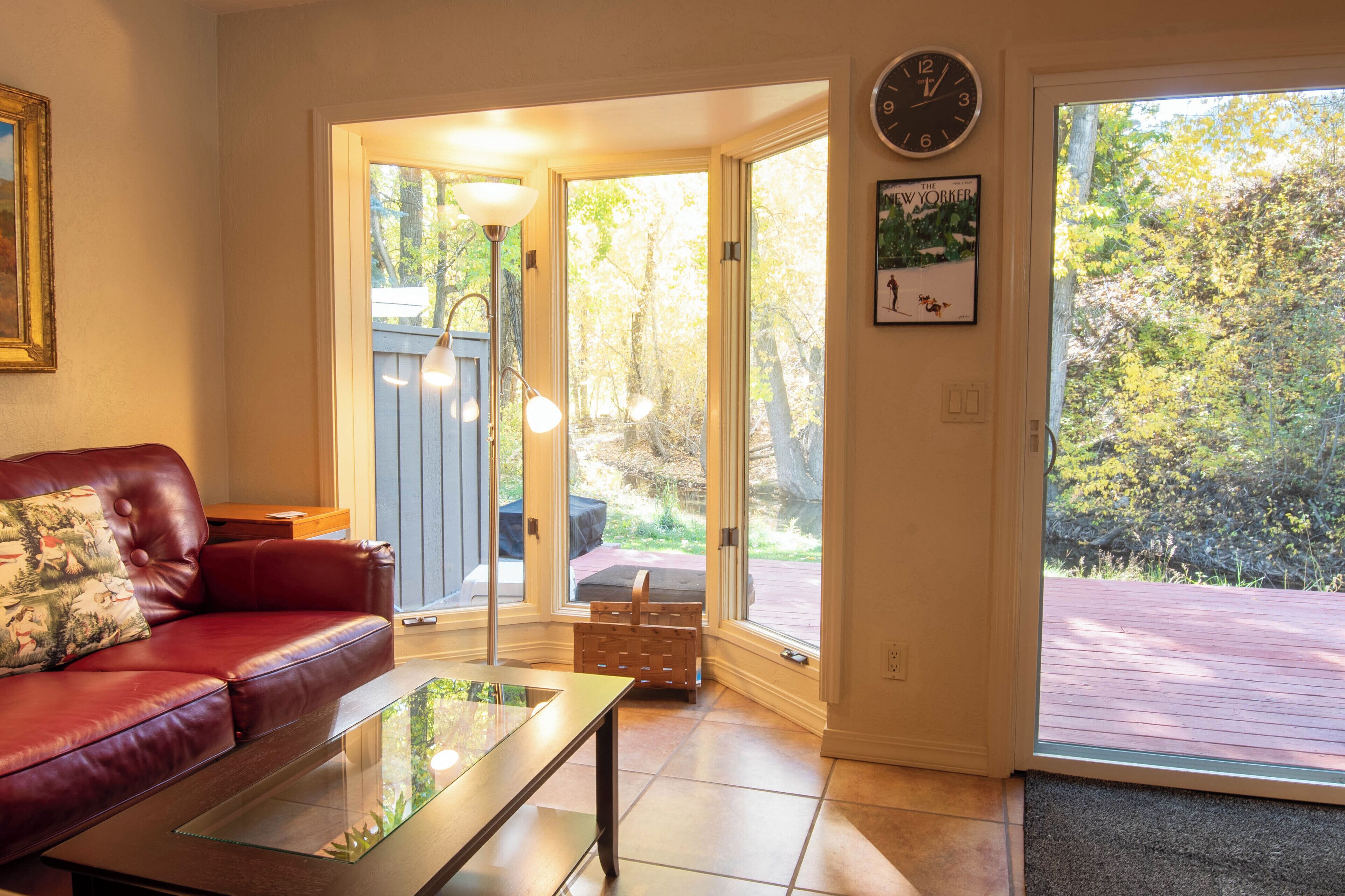 A living room with a red leather sofa, a glass coffee table, and a door leading to an outdoor deck.