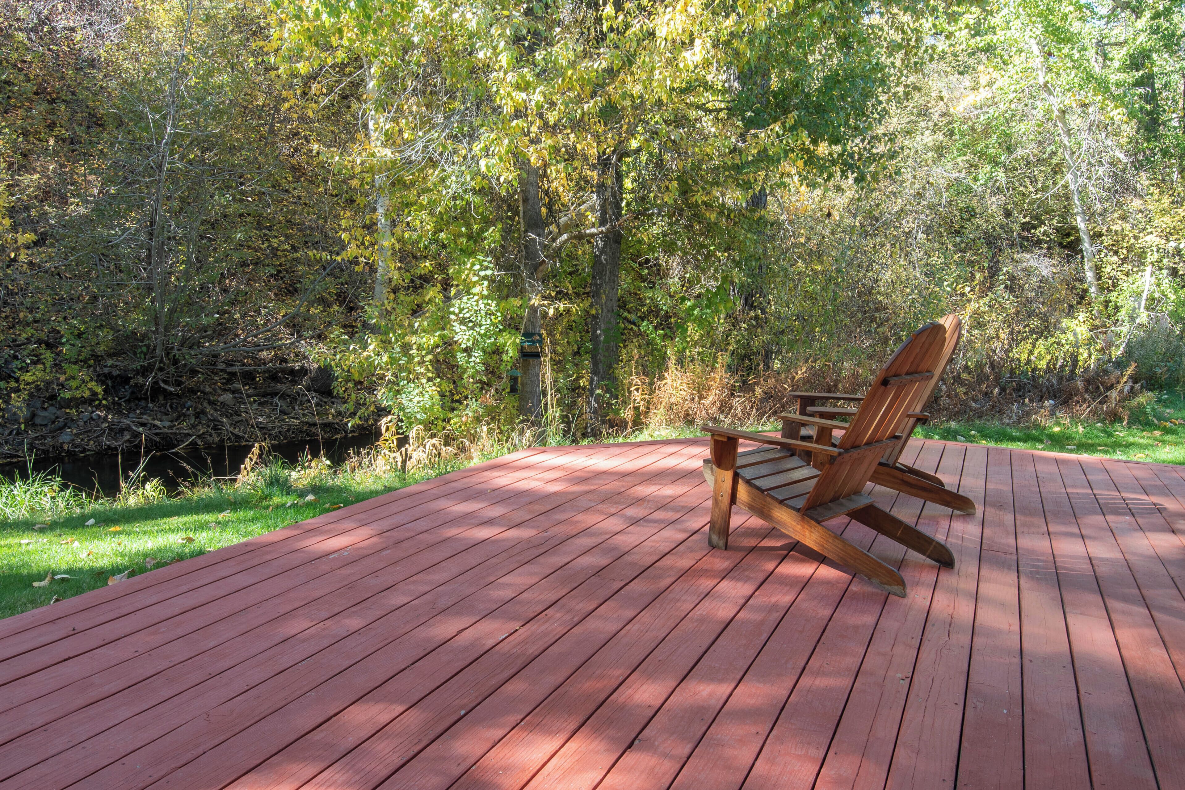 A wooden rocking chair on a red deck surrounded by trees.