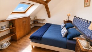 A bedroom with a sloped ceiling, a skylight, a bed with blue bedding, wooden furniture, and a small bedside table with a lamp.