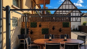 An outdoor patio with a round wooden table and chairs, a wooden fence, and a view of a traditional building in the background.