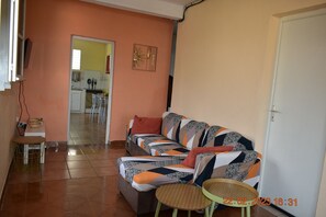 Ein Wohnzimmer mit einer Couch, zwei kleinen Tischen, einer Tür und einer Küche im Hintergrund.