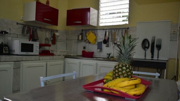 Een keuken met witte kastjes, een magnetron en een fruitschaal met bananen en een ananas op een rode schaal.