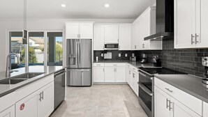 A modern kitchen with white cabinets, stainless steel appliances, and a tiled backsplash.