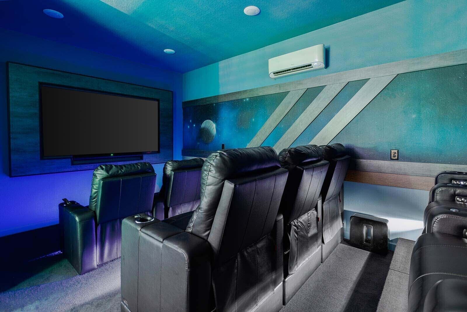 Ein Heimkino mit großer Leinwand, bequemen Ledersesseln und einer Klimaanlage an der Wand.