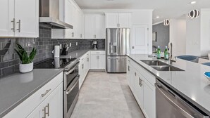 A modern kitchen with white cabinets, stainless steel appliances, and a grey tiled backsplash. - Rhythmic Retreat | Beach + music lover's oasis w pool, movie theater, karaoke rm (Melbourne Beach)