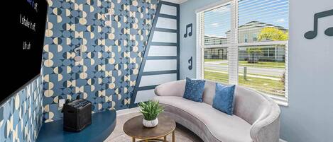 Una sala de estar moderna con un sofá gris curvo, una mesita redonda con una planta y una pared con un patrón geométrico.